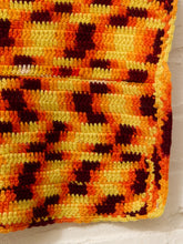 Load image into Gallery viewer, A close-up of a crocheted or knitted textile with a repeating pattern in yellow, orange, and dark brown, shown against a white textured background.
