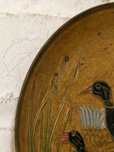 Load image into Gallery viewer, Close-up of an oval decorative wall plaque featuring two ducks and reeds on a textured gold background, set against a white stone wall.
