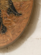 Load image into Gallery viewer, Close-up detail of a round bronze-toned decorative object with embossed black and gold bird-like artwork, resting against a light textured surface.

