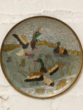Load image into Gallery viewer, A round decorative wall plaque featuring an embroidered or needlepoint scene of mallards in a pond, mounted on a white textured brick wall.
