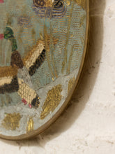 Load image into Gallery viewer, Close-up of an oval decorative wall mirror with a hand-painted nature scene featuring ducks, reeds, and gold leaf accents, mounted on a textured white plaster wall.
