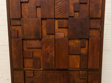 Load image into Gallery viewer, A dark brown wooden wall cabinet or decorative cabinet featuring an abstract geometric pattern of raised rectangular panels in varying wood tones, set against a white brick wall.
