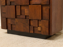 Load image into Gallery viewer, A close-up of a mid-century modern wooden sideboard or cabinet with a geometric, block-like facade design in rich dark brown wood, resting on a black metal base over a beige carpet.
