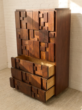 Load image into Gallery viewer, Mid-century modern wooden chest of drawers with an abstract geometric block design, featuring a dark brown finish and one open drawer showing a lighter wood interior, set against a white brick wall.
