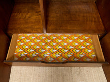 Load image into Gallery viewer, A wooden drawer pulled open, showing a colorful retro patterned paper liner with orange, yellow, white, and black wavy shapes.
