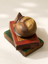 Load image into Gallery viewer, A carved wooden decorative object resembling a stylized fruit or abstract form, displayed on top of two stacked vintage-style books against a light fabric background.
