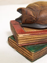 Load image into Gallery viewer, A close-up of a carved wooden cat figurine resting on top of stacked vintage-style books with red, brown, and green painted covers, set against a plain light background.

