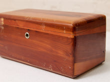 Load image into Gallery viewer, A rectangular wooden box with a hinged lid, made of reddish-brown wood with visible grain and wear, photographed on a light fabric surface.
