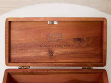 Load image into Gallery viewer, An open wooden storage box or cabinet lid made of medium brown wood, with engraved branding reading 'Lane Cedar Cabinets' and 'Schoen's Furniture Ortonville Minnesota.' The box is photographed against a light neutral background.
