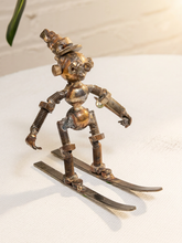 Load image into Gallery viewer, A handmade metal sculpture of a whimsical, rusty robot skier wearing a top hat and standing on metal skis, displayed on a white textured surface.
