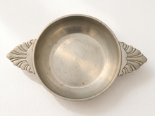 Load image into Gallery viewer, A vintage silver-toned metal bowl with decorative shell-shaped side handles, shown on a white textured fabric background.
