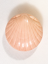 Load image into Gallery viewer, A carved shell-shaped decorative object in a pale peach-pink color, photographed from above on a textured off-white background.

