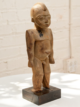 Load image into Gallery viewer, A hand-carved wooden statue of a standing figure with a dark base, photographed indoors against a white brick wall and white tabletop.
