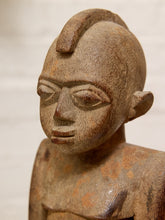 Load image into Gallery viewer, A close-up of a carved wooden statue with a stylized face, textured finish, and reddish-brown patina, set against a soft neutral background.
