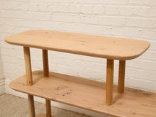 Load image into Gallery viewer, A light natural wood two-tier shelf with rounded rectangular tops and four legs, set against a white painted brick wall.

