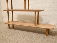 Load image into Gallery viewer, A light natural wood two-tier shelf with a minimalist mid-century modern design, standing on a textured beige rug against a white painted brick wall.
