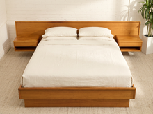 Load image into Gallery viewer, A modern platform bed with a light brown wood frame, matching headboard and side tables, dressed in white bedding, set against a white brick wall and beige carpet.
