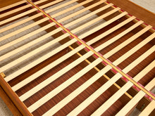 Load image into Gallery viewer, Close-up of a wooden bed frame slatted base with light natural wood slats over a darker reddish-brown wood backing, photographed indoors on a carpeted floor.
