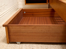 Load image into Gallery viewer, A close-up of a wooden storage drawer with casters, shown partially open on a textured beige carpet in an indoor setting.
