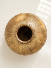 Load image into Gallery viewer, A top-down view of a round ceramic vase with a metallic gold and bronze glaze, set against a plain off-white background with soft window shadow patterns.
