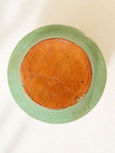 Load image into Gallery viewer, Top-down view of a round ceramic plate or dish with a light green glazed rim and a warm orange-brown unglazed center, photographed on a light fabric background.
