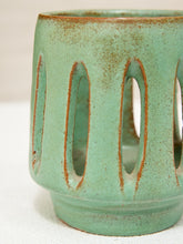 Load image into Gallery viewer, A close-up of a ceramic cup or candle holder with a textured sage green glaze and brown speckled edges, featuring vertical oval cutouts on the side.
