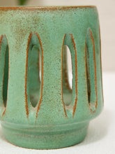 Load image into Gallery viewer, Close-up of a ceramic cup or candle holder with a textured sage green glaze and vertical oval cutouts, showing a warm brown clay edge.
