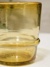 Load image into Gallery viewer, A close-up of a translucent amber glass tumbler with a flared rim and small air bubbles visible inside, set against a light neutral background.
