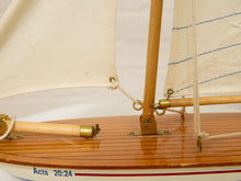 Load image into Gallery viewer, Close-up of a wooden model sailboat with cream-colored canvas sails, a polished wooden deck, brass fittings, and a white hull with blue text reading 'Acts 20:24'.
