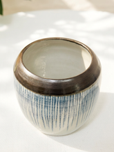 Load image into Gallery viewer, A handmade ceramic planter pot with a wide, dark brown rim and a textured body featuring vertical blue brushstrokes on an off-white base, set on a white fabric surface with soft natural shadows.

