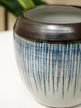 Load image into Gallery viewer, Close-up of a ceramic vase with a dark brown glazed rim and vertical blue brushstroke patterns on a white body, set against a softly blurred background.
