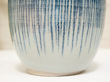 Load image into Gallery viewer, Close-up of a ceramic vase or cup with a glossy white glaze and vertical blue brushstroke pattern, shown against a soft neutral background.
