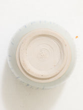 Load image into Gallery viewer, Top-down view of a ceramic cup or small bowl showing the unglazed beige clay base with a circular stamp mark, surrounded by a pale blue glazed rim with faint blue dashed lines, on a white background.
