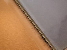 Load image into Gallery viewer, Close-up of a spiral-bound notebook with a textured tan leather cover on the left and a smooth gray cover on the right, bound by a gold-toned metal spiral.
