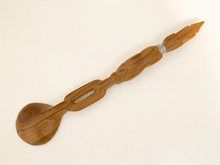 Load image into Gallery viewer, A handcrafted wooden spoon with a decorative handle, featuring a carved design and a small silver metal accent ring, shown on a textured off-white background.

