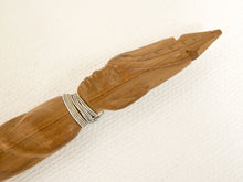 Load image into Gallery viewer, A close-up of a carved wooden object, likely a decorative pen or tool, featuring a detailed face carving on the handle and a silver-colored wire wrap around the neck, set against a textured off-white background.
