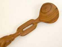 Load image into Gallery viewer, A handcrafted wooden spoon with a unique handle featuring a rectangular cutout, resting diagonally on a textured off-white fabric background.
