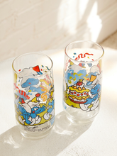 Load image into Gallery viewer, Two clear glass tumblers with colorful cartoon Smurf illustrations, photographed on a sunlit white surface with a white wall background.
