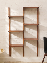 Load image into Gallery viewer, A pair of mid-century modern wooden ladder shelves mounted on a white brick wall, with one shelf on the left featuring four tiers and one on the right featuring five tiers. A small side table with a glass and a black chair are partially visible in the foreground.

