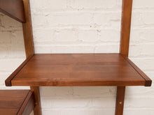 Load image into Gallery viewer, A close-up of a mid-century modern wooden shelving unit with a warm medium-brown finish, featuring a shelf panel and vertical support posts against a white brick wall.
