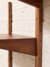 Load image into Gallery viewer, Close-up of a wooden wall-mounted shelf with a medium brown finish, showing the shelf panel and vertical support posts against a white painted brick wall.
