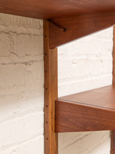 Load image into Gallery viewer, Close-up of a mid-century modern wooden shelf with a warm brown finish, mounted against a white painted brick wall.
