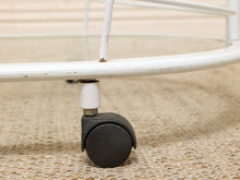 Load image into Gallery viewer, Close-up of a black caster wheel attached to a white metal frame, resting on a woven beige rug.
