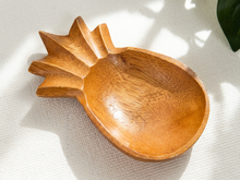 Load image into Gallery viewer, A hand-carved wooden bowl shaped like a pineapple, made from warm medium-brown wood with visible grain, resting on a textured white fabric surface with soft natural shadows.

