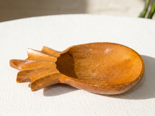 Load image into Gallery viewer, A hand-carved wooden bowl with a stylized leaf or flower-like handle, resting on a textured white fabric surface.
