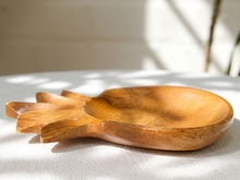 Load image into Gallery viewer, A hand-carved wooden spoon with a bowl and three handle prongs, resting on a textured white fabric surface with soft, dappled sunlight and shadows.
