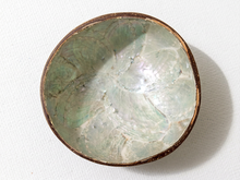 Load image into Gallery viewer, A handmade bowl with a natural brown wooden rim and an iridescent green-blue abalone shell interior, photographed from a top-down angle on a white textured background.
