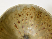 Load image into Gallery viewer, Close-up of the interior of a ceramic bowl with a glossy, mottled glaze in earthy olive-green and beige tones, decorated with numerous small brown speckles and a darker smoky area near the bottom center.
