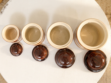 Load image into Gallery viewer, Five small ceramic jars with matching lids arranged by size on a round white surface. The jars are cream-colored on the inside and exterior, while the lids are glossy dark brown.
