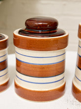 Load image into Gallery viewer, A close-up of a ceramic canister with a matching lid, featuring horizontal stripes in brown, cream, and blue, set against a neutral background.
